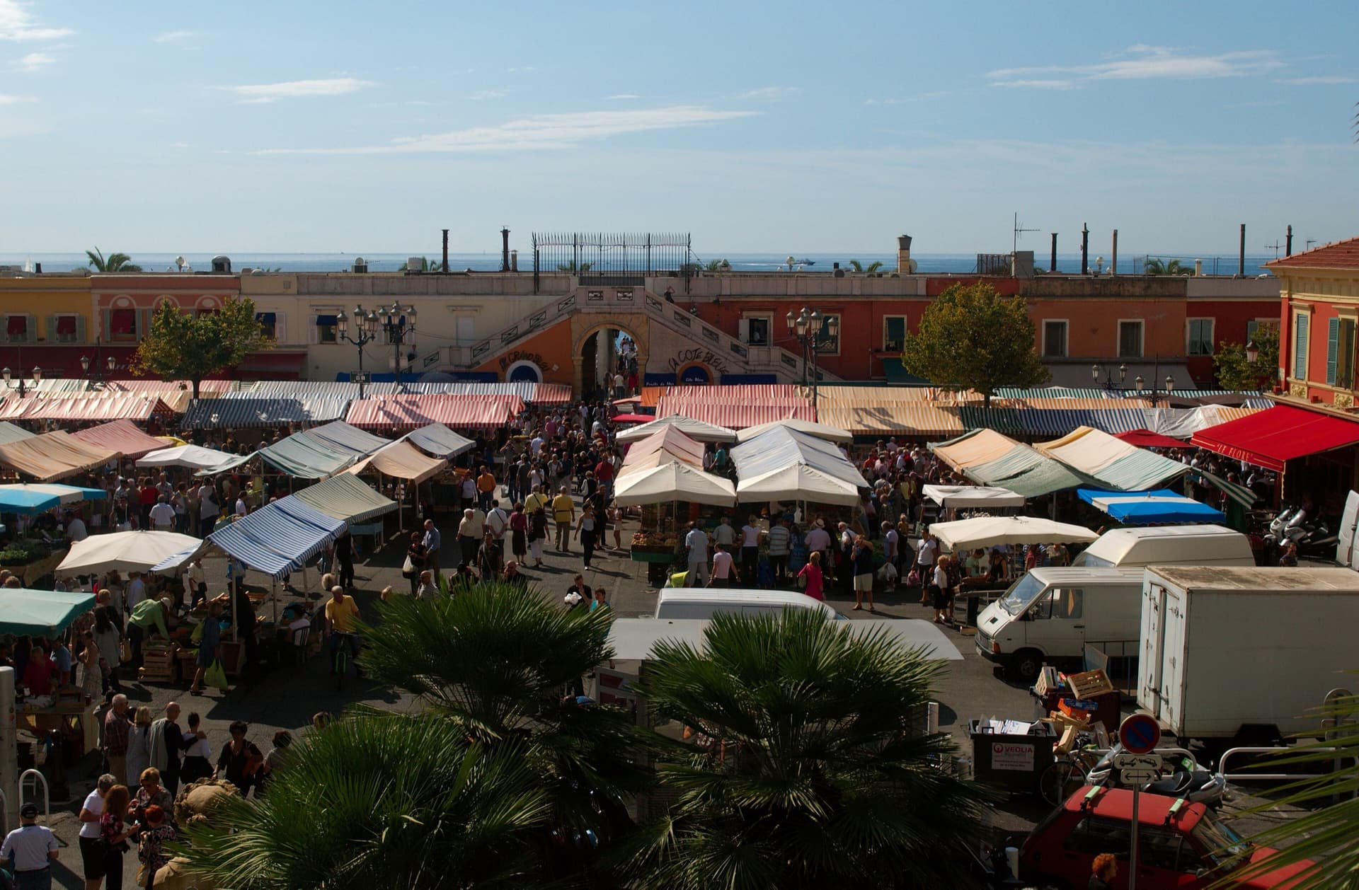The cours Saleya market in the Old Town of Nice, its stalls under striped awnings with the sea behind.